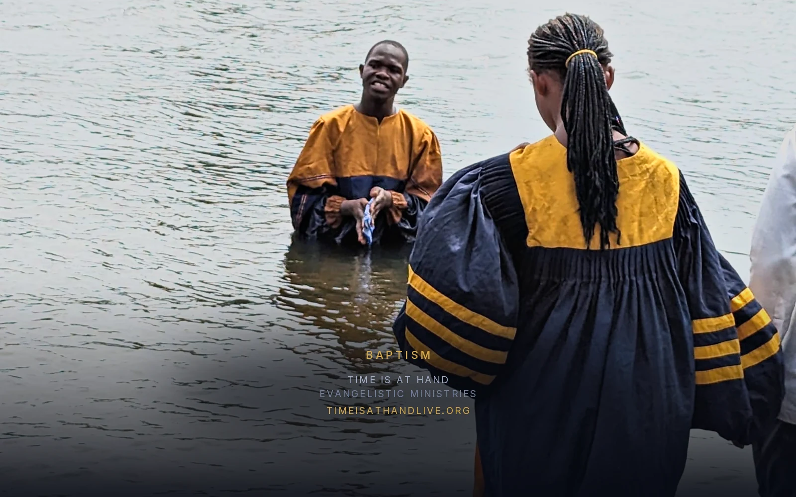 A candidate in a baptismal gown wading out to the minister waiting in the river