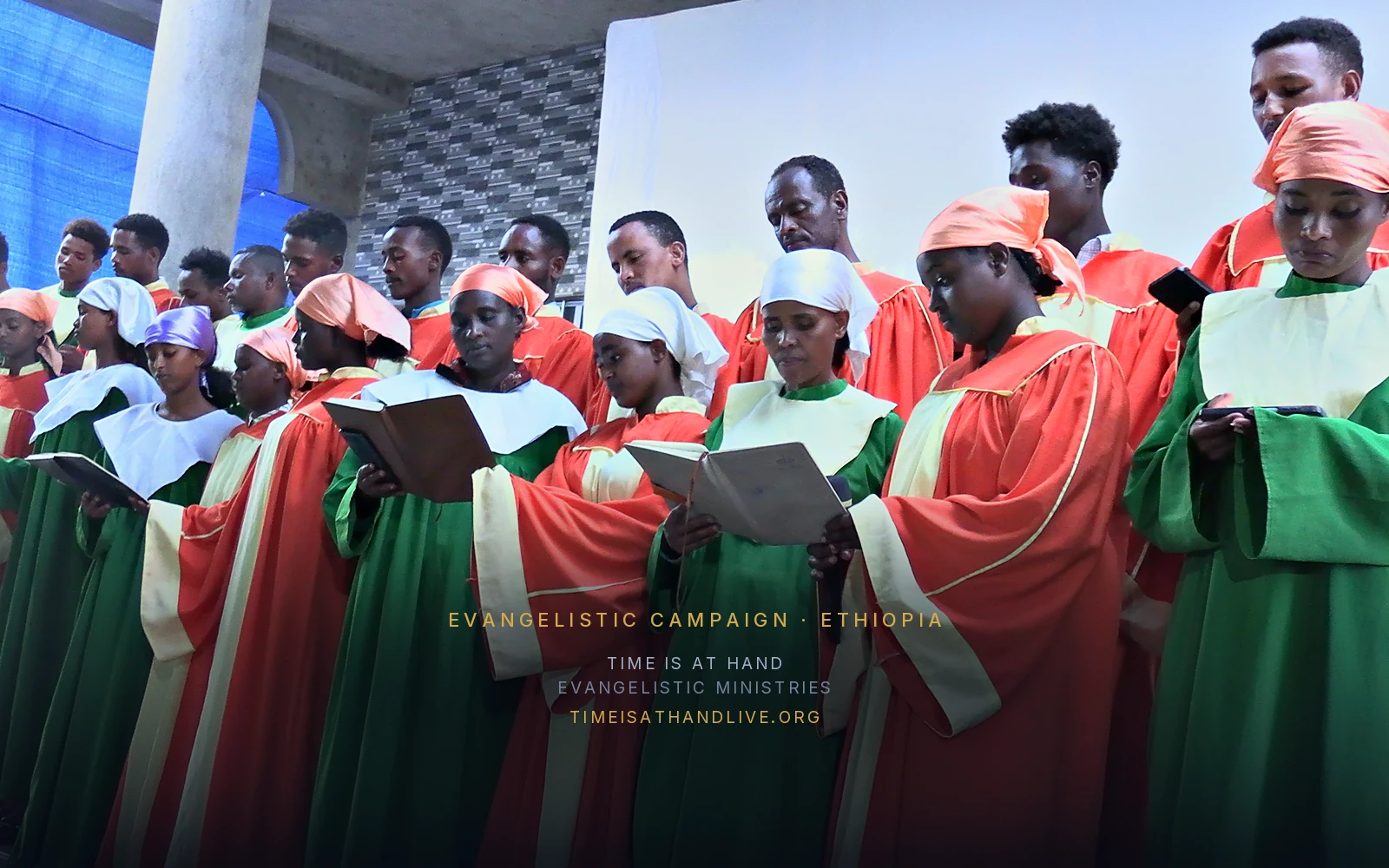 The choir singing in scarlet and green vestments