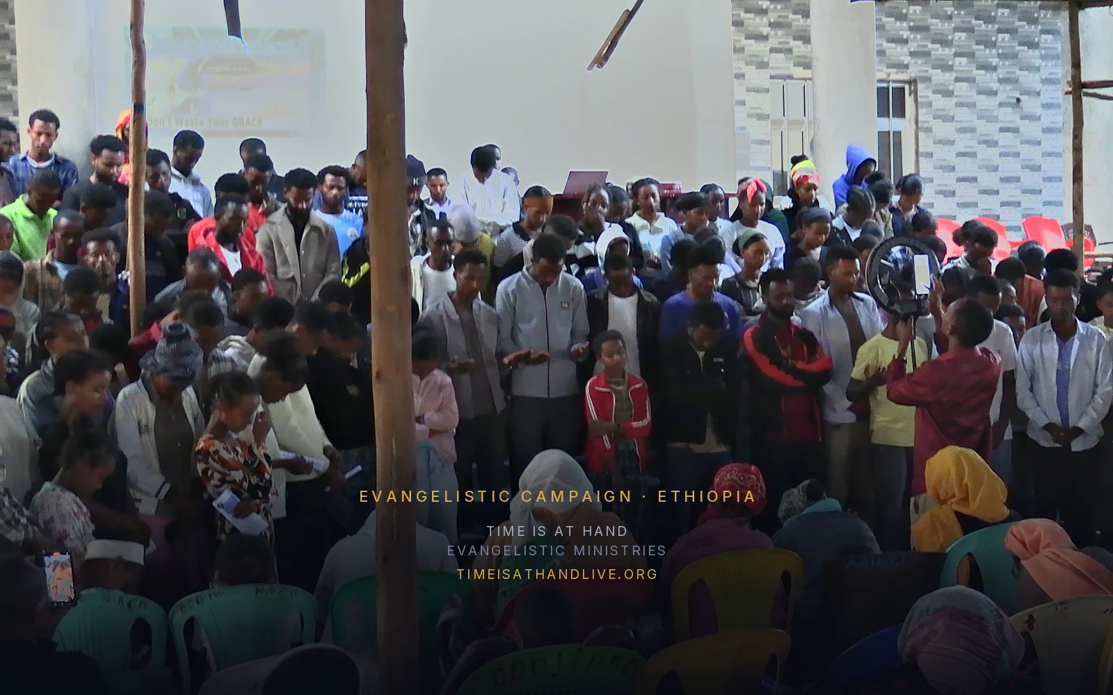 The congregation standing in prayer, hands raised, the projection screen lit behind them