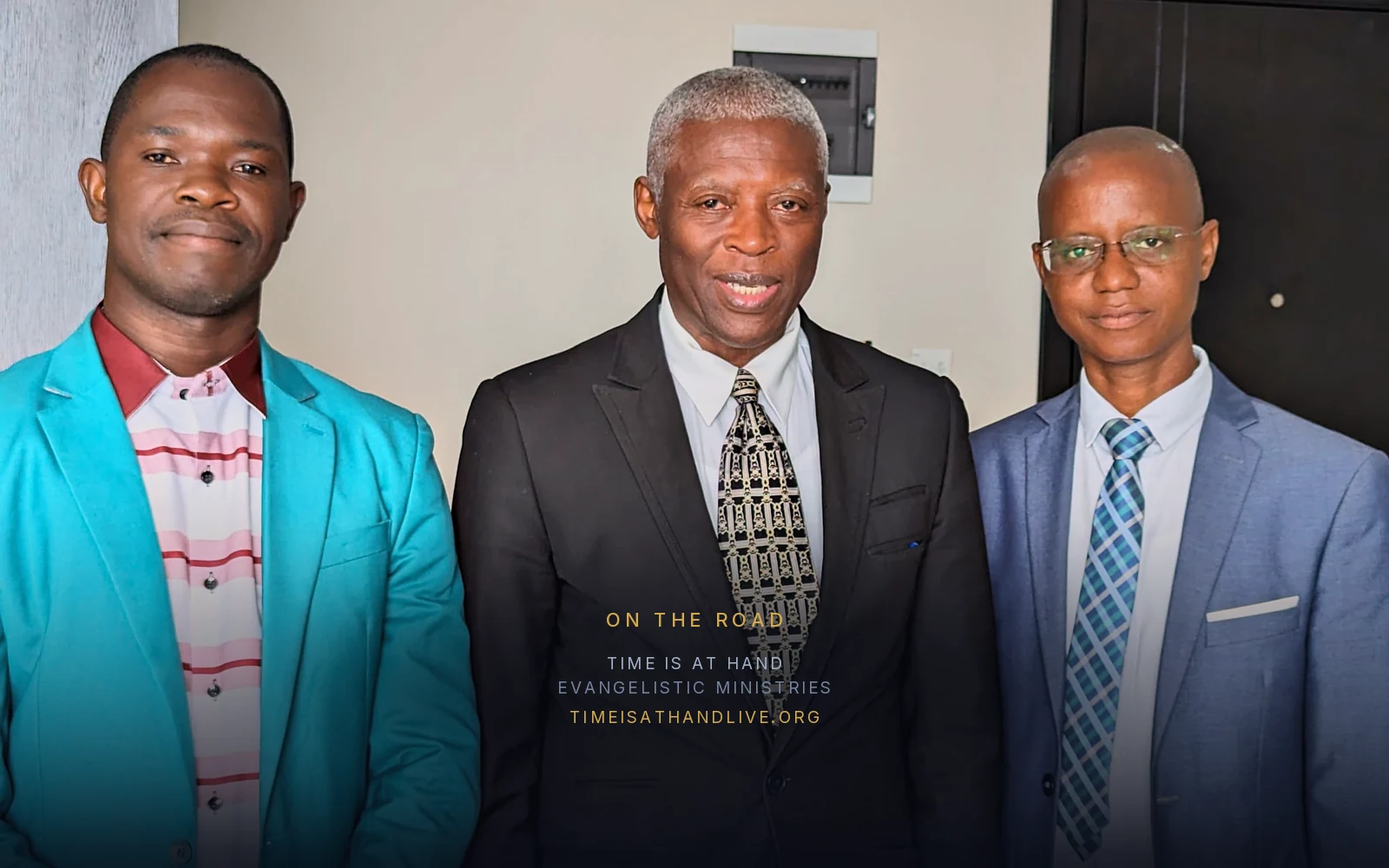 Devon Searchwell standing between two ministers, one in a turquoise jacket and one in blue